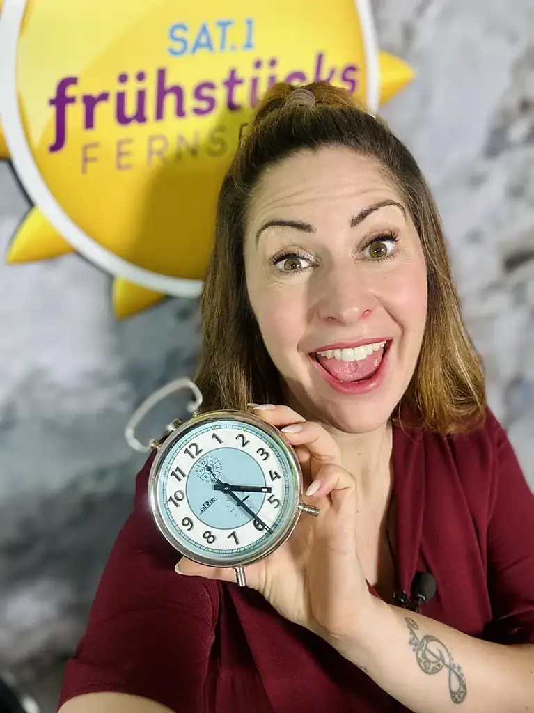 Moderatorin Madita van Hülsen hält einen Wecker in die Kamera, dahinter die Sonne des SAT.1-Frühstücksfernsehens