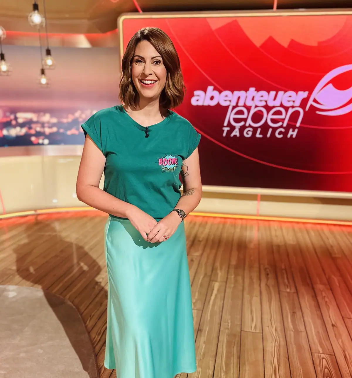 Madita van Hülsen steht im Fernsehstudio von „Abenteuer Leben täglich“ vor der beleuchteten Sendungstafel