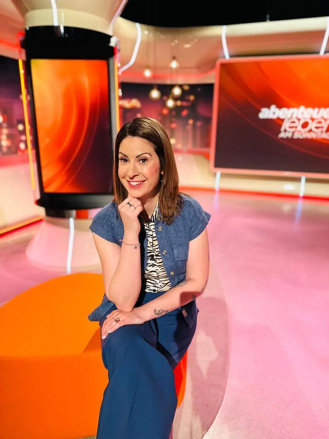 Moderatorin Madita van Hülsen sitzt lächelnd im TV-Studio von „Abenteuer Leben“